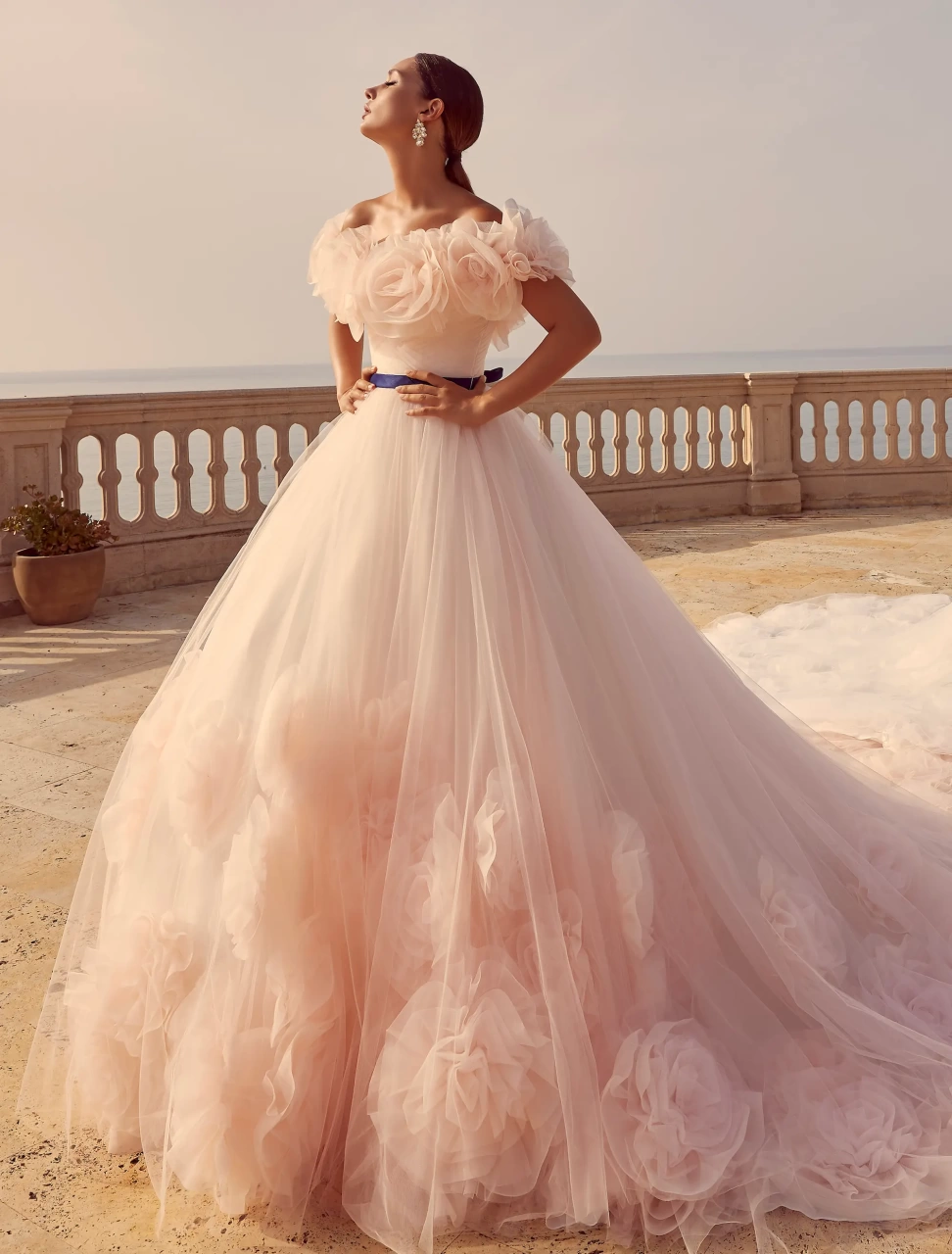 Abito da sposa particolare colorato rosa lussuoso e principesco in tulle, scollo off-shoulder con grandi rose di tulle applicate sia davanti che sulla schiena, fascia in raso viola in vita, gonna ampia in tulle con lavorazione di grandi rose tridimensionali di tulle, disponibile anche in bianco | Lo Specchio Atelier Abiti da Sposa a Verona