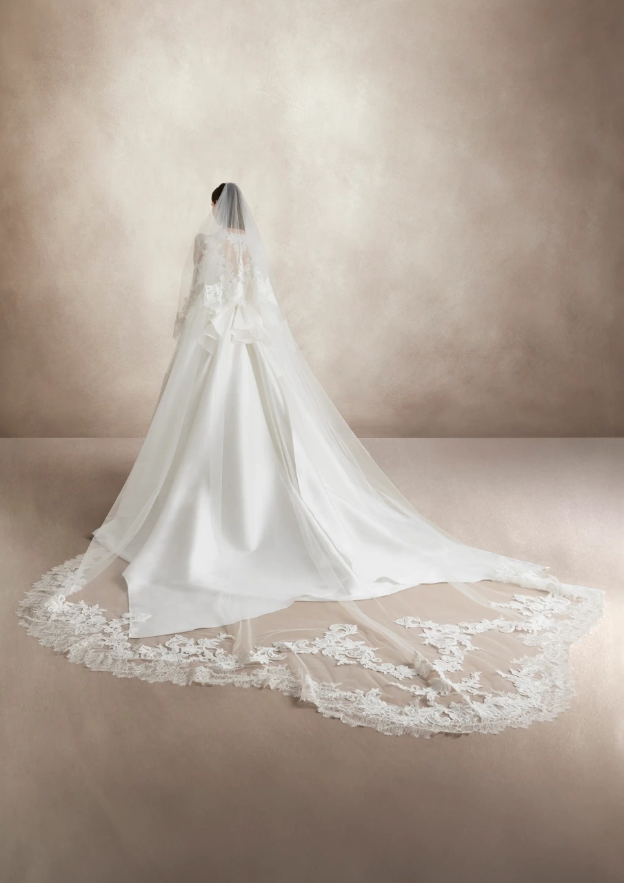 Abito da sposa particolare con maniche lunghe a sbuffo in pizzo effetto tattoo, scollo rotondo, gonna ampia A-line drappeggiata in mikado con fiocco drappeggiato sulla schiena e strascico lungo