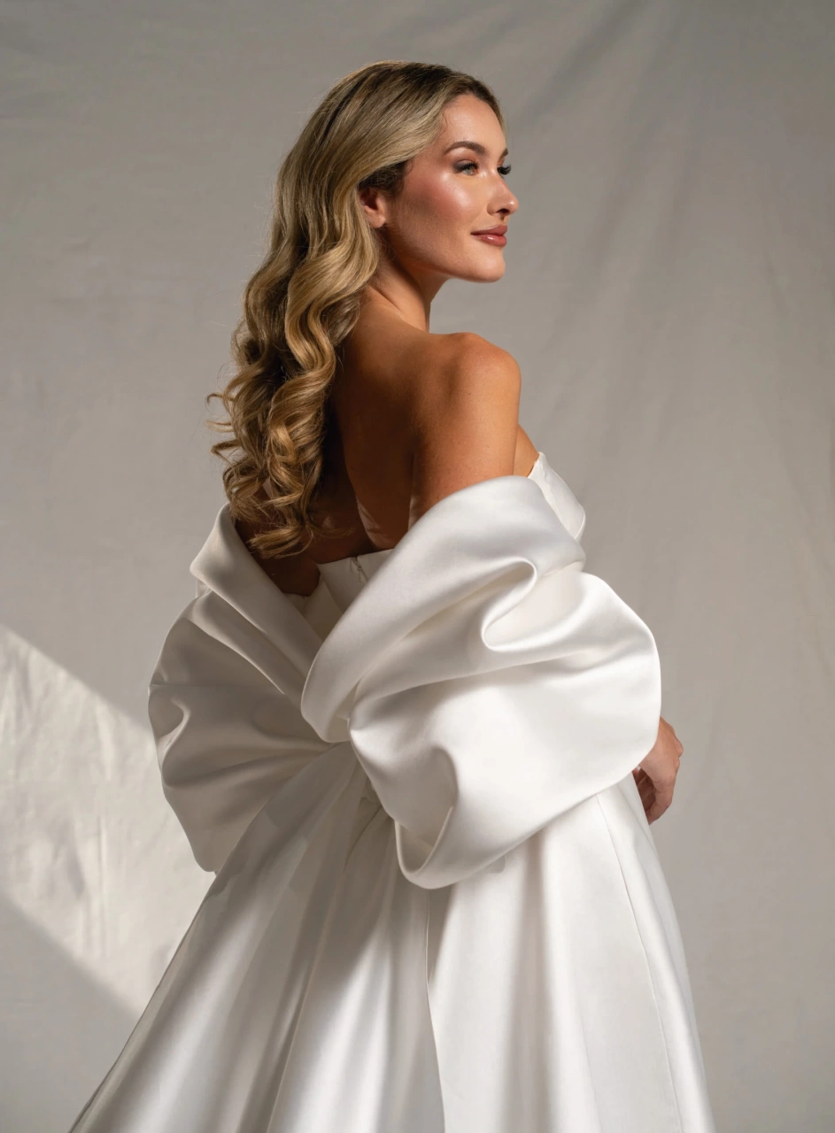 Abito da sposa semplice A-line in mikado lucido, scollo dritto senza spalline, dettaglio particolare di fiocco grande sulla schiena che funge da maniche grandi e voluminose