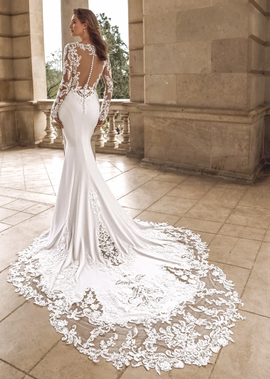 Abito da sposa particolare a sirena in crepe, maniche lunghe e schiena scoperta in pizzo effetto tattoo, fianchi cut-out in pizzo, strascico particolare drammatico con lavorazioni in pizzo