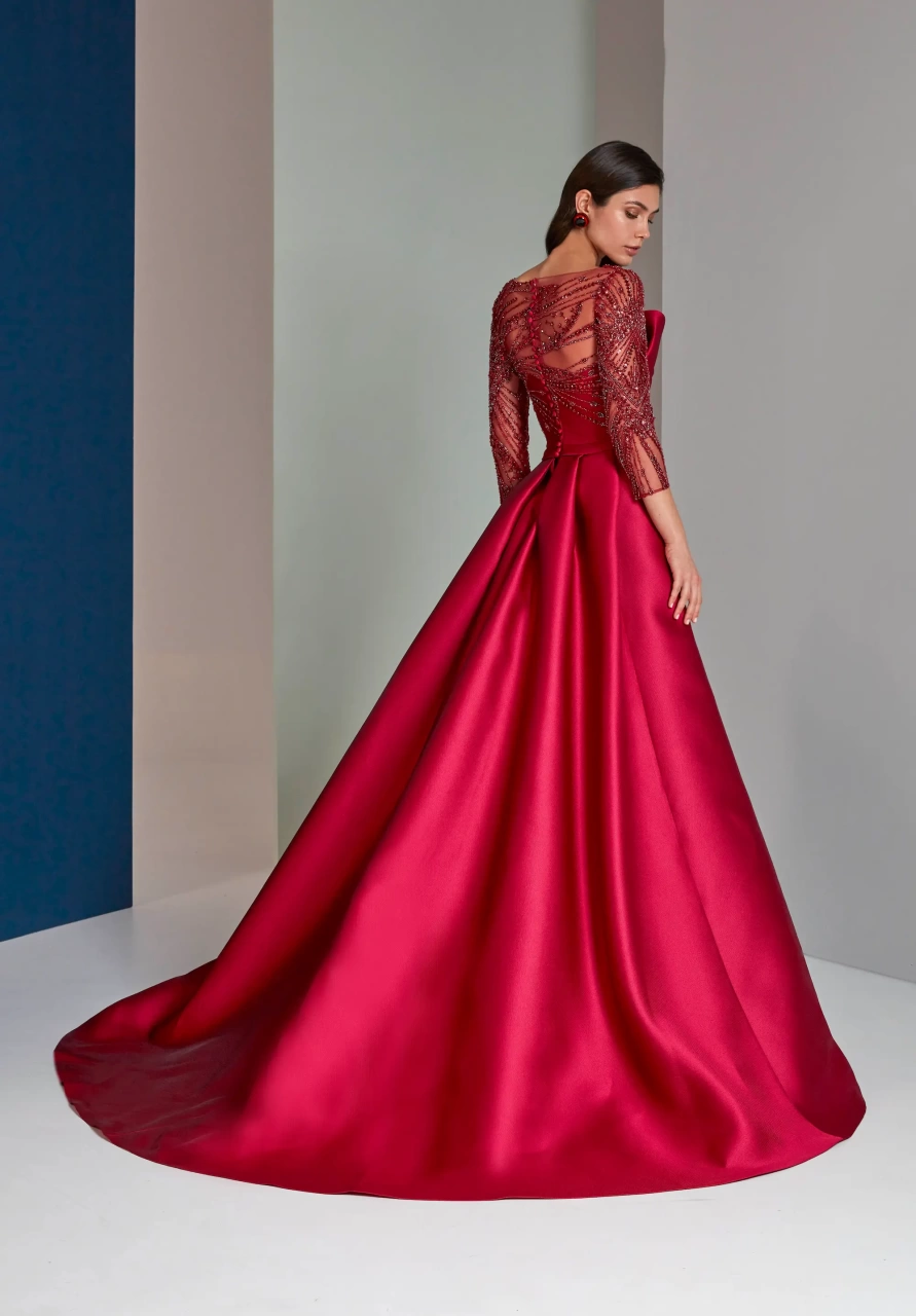 Abito rosso da cerimonia con maniche lunghe velate con applicazioni di strass e cristalli ton-sur-ton, scollo a barchetta velato, bustino drappeggiato, gonna midi asimmetrica con strascico strutturato voluminoso - Lo Specchio Atelier Abiti da Cerimonia a Verona