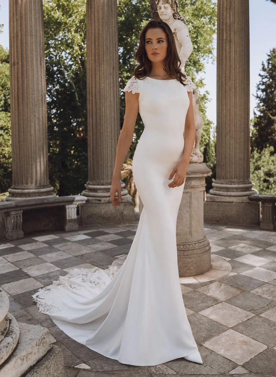 Abito da sposa con maniche corte in pizzo effetto tattoo, schiena scoperta, scollo a barchetta, strascico particolare con lavorazione in pizzo