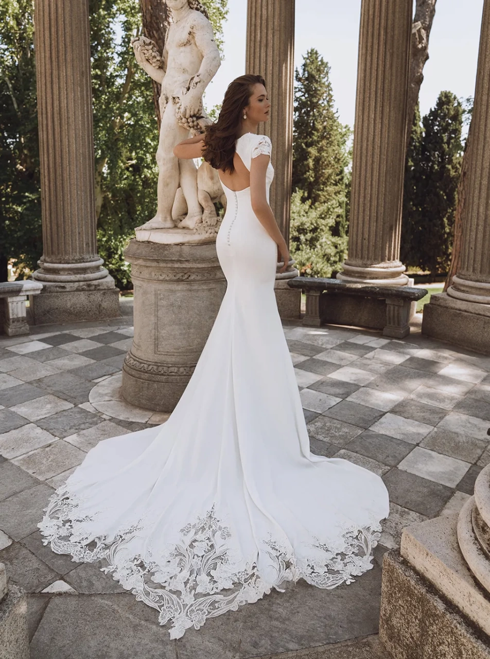 Abito da sposa con maniche corte in pizzo effetto tattoo, schiena scoperta, scollo a barchetta, strascico particolare con lavorazione in pizzo