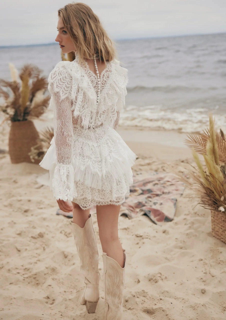 Abito da sposa corto particolare stile boho country in pizzo, maniche lunghe a campana effetto tattoo, colletto alto in pizzo, gonna a balze, lavorazione di balze in pizzo sullo scollo