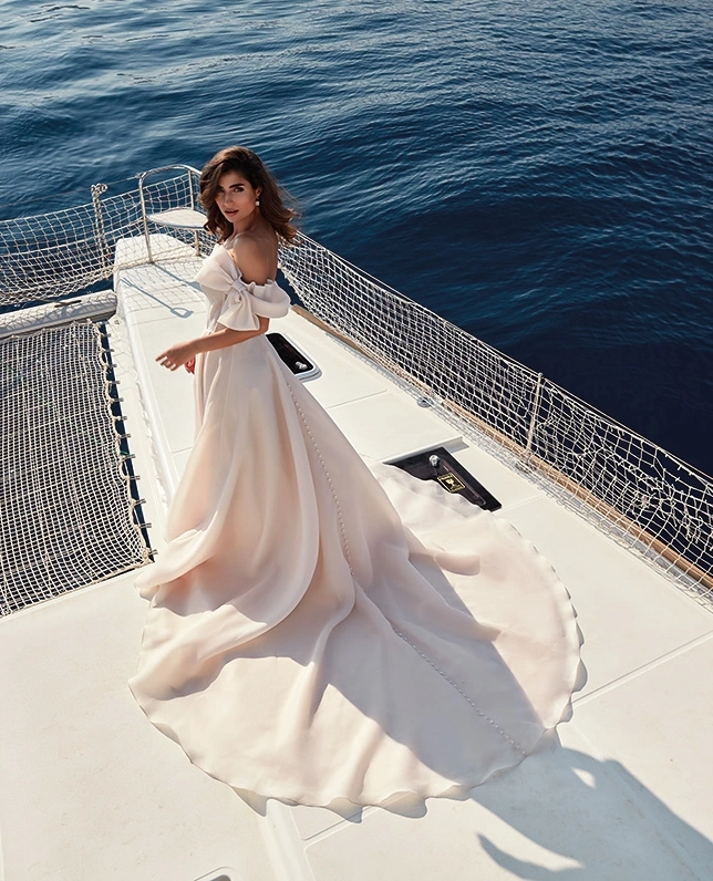 Abito da sposa classico semplice elegante e raffinato con scollo dritto off-shoulder, fiocco strutturato sulla spallina sinistra, corsetto con stecche a vista e lavorazione di piccoli glitter e cristalli, gonna scivolata in organza con spacco a portafoglio | Lo Specchio Atelier Abiti da Sposa a Verona