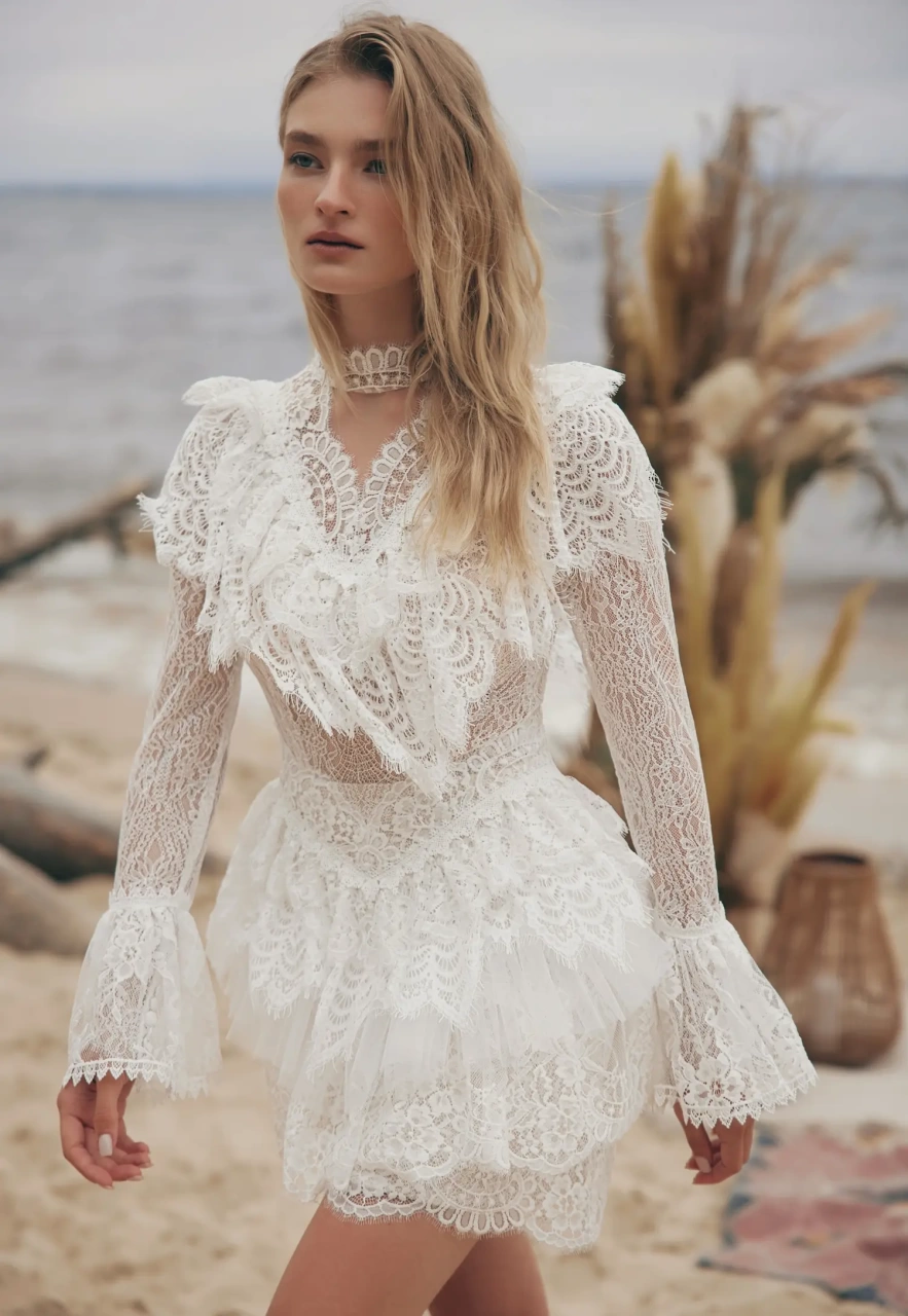 Abito da sposa corto particolare stile boho country in pizzo, maniche lunghe a campana effetto tattoo, colletto alto in pizzo, gonna a balze, lavorazione di balze in pizzo sullo scollo