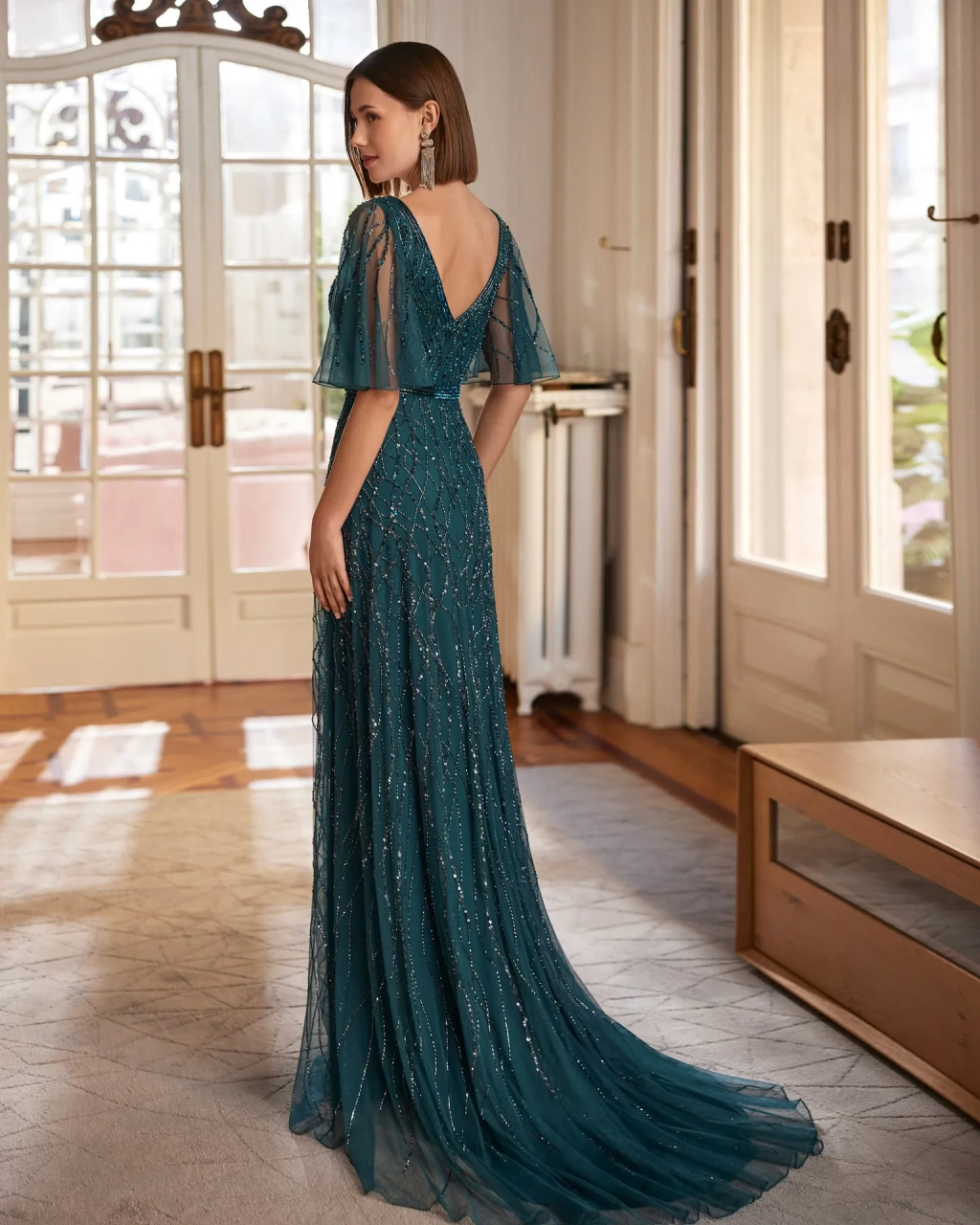 Abito da cerimonia lungo verde scuro A-line con scollo a V sia davanti che dietro, maniche corte velate a campana, trama con applicazioni di strass e glitter su tutta la silhouette - Lo Specchio Sposi Atelier Abiti da Cerimonia a Verona