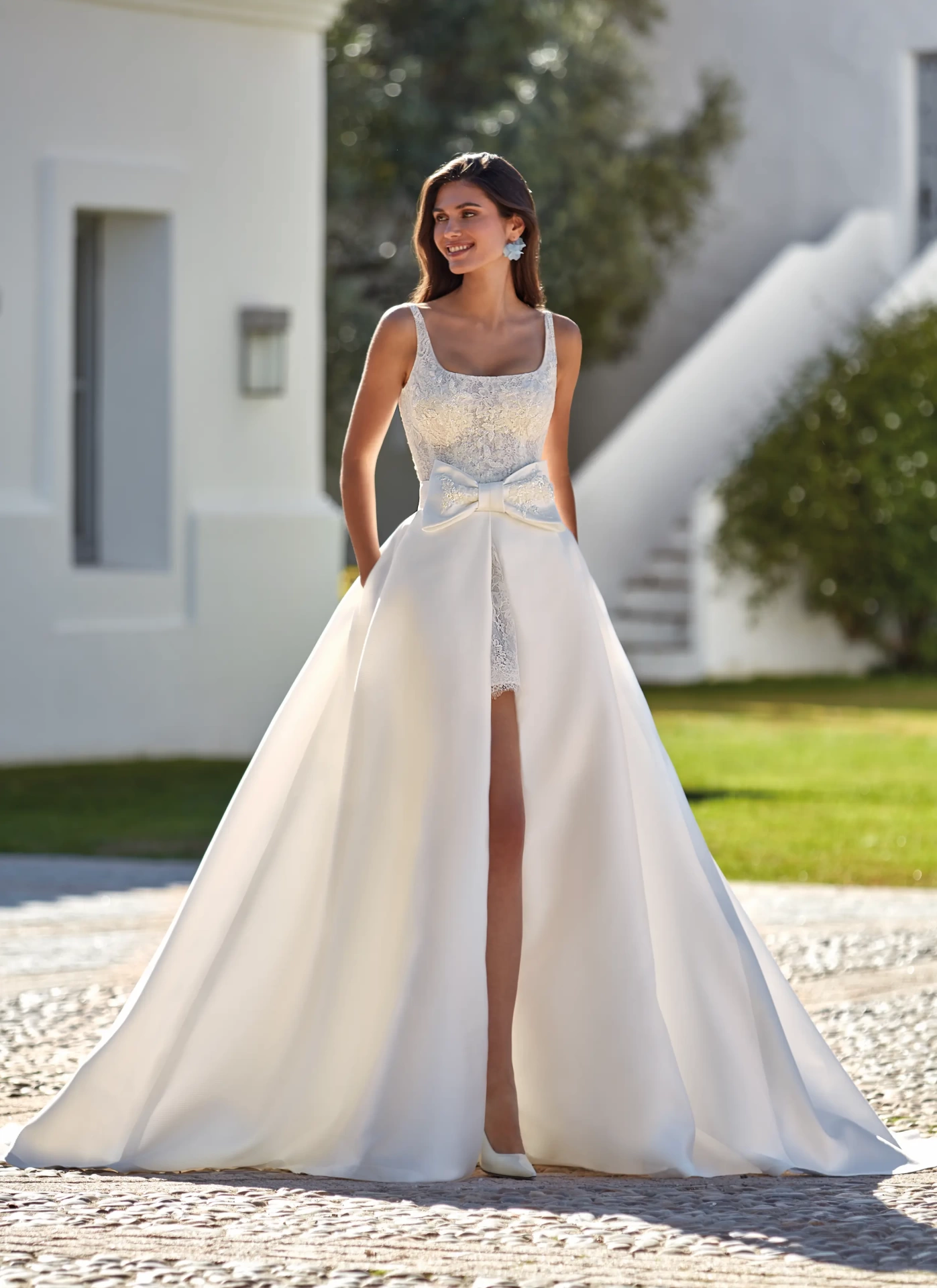 Vestito da sposa corto in pizzo con scollo squadrato e spalline spesse, gonna staccabile ampia e strutturata in mikado con fiocco frontale in pizzo