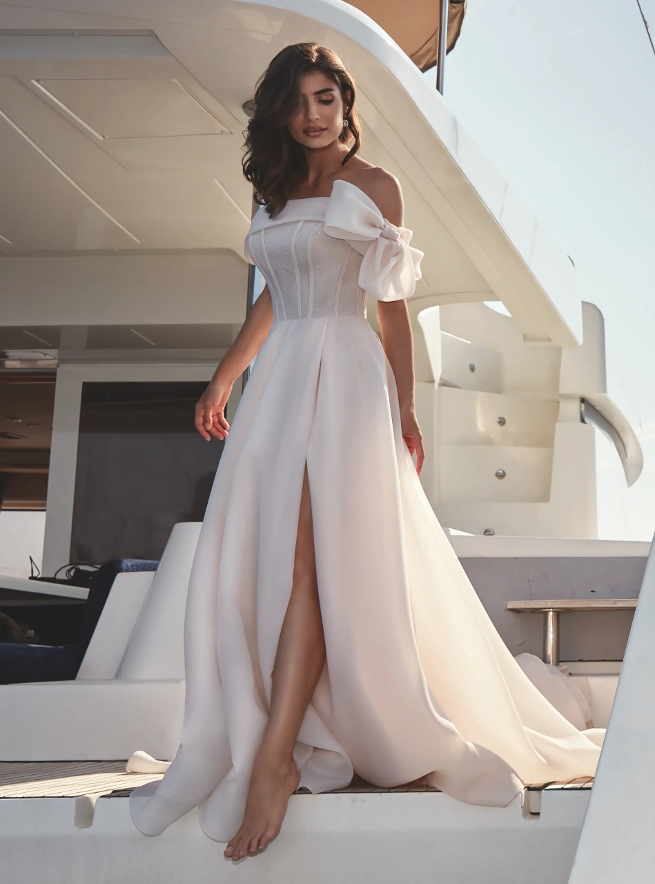 Abito da sposa classico semplice elegante e raffinato con scollo dritto off-shoulder, fiocco strutturato sulla spallina sinistra, corsetto con stecche a vista e lavorazione di piccoli glitter e cristalli, gonna scivolata in organza con spacco a portafoglio | Lo Specchio Atelier Abiti da Sposa a Verona