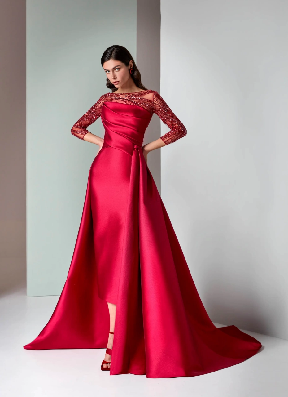 Abito rosso da cerimonia con maniche lunghe velate con applicazioni di strass e cristalli ton-sur-ton, scollo a barchetta velato, bustino drappeggiato, gonna midi asimmetrica con strascico strutturato voluminoso - Lo Specchio Atelier Abiti da Cerimonia a Verona