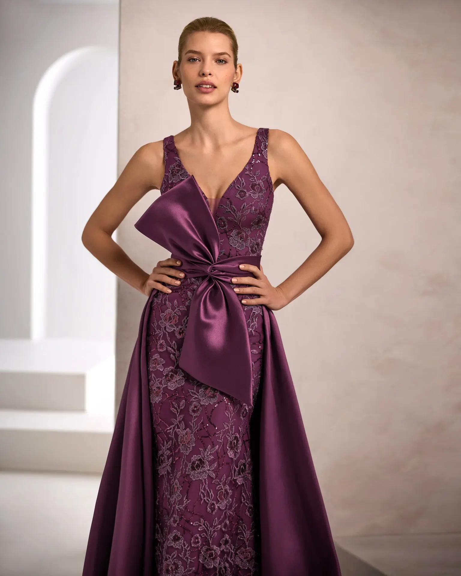 Vestito da cerimonia elegante da donna lungo viola in pizzo floreale, scollo profondo a V e spalline larghe, con sovragonna ampia in mikado viola con fiocco scenografico sul punto vita - Lo Specchio Atelier Abiti da Cerimonia a Verona