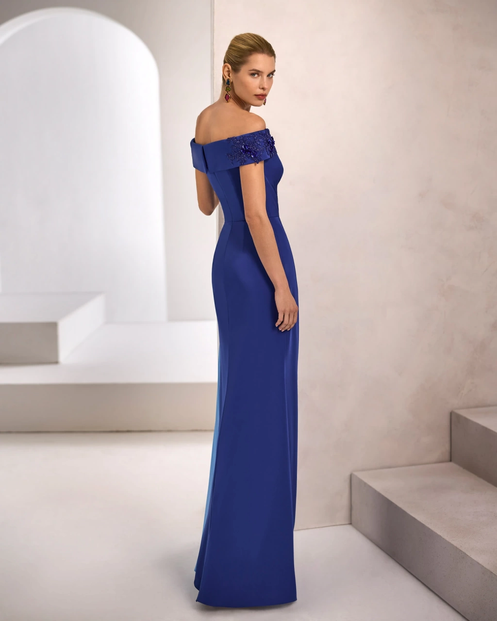 Vestito da cerimonia donna lungo blu, scollo off-shoulder strutturato, drappeggio sul punto vita e gonna asimmetrica a contrasto, applicazioni 3D di pizzo floreale sulla spalla destra e sul corpetto - Lo Specchio Atelier Abiti da Cerimonia a Verona