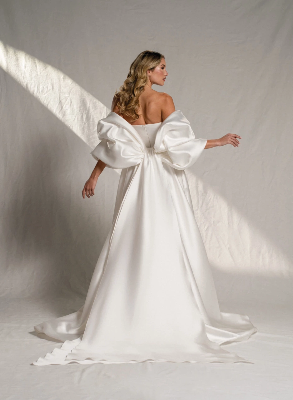 Abito da sposa semplice A-line in mikado lucido, scollo dritto senza spalline, dettaglio particolare di fiocco grande sulla schiena che funge da maniche grandi e voluminose