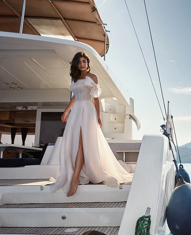 Abito da sposa classico semplice elegante e raffinato con scollo dritto off-shoulder, fiocco strutturato sulla spallina sinistra, corsetto con stecche a vista e lavorazione di piccoli glitter e cristalli, gonna scivolata in organza con spacco a portafoglio | Lo Specchio Atelier Abiti da Sposa a Verona