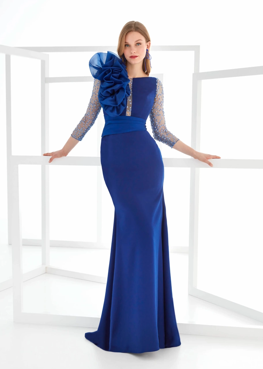 Abito da cerimonia blu elettrico con maniche lunghe velate con applicazioni di cristalli, silhouette a sirena, scollo a barchetta con dettaglio velato, fascia drappeggiata sul punto vita, ruches 3D voluminose e scenografiche sulla spalla destra - Lo Specchio Atelier Abiti da Cerimonia a Verona