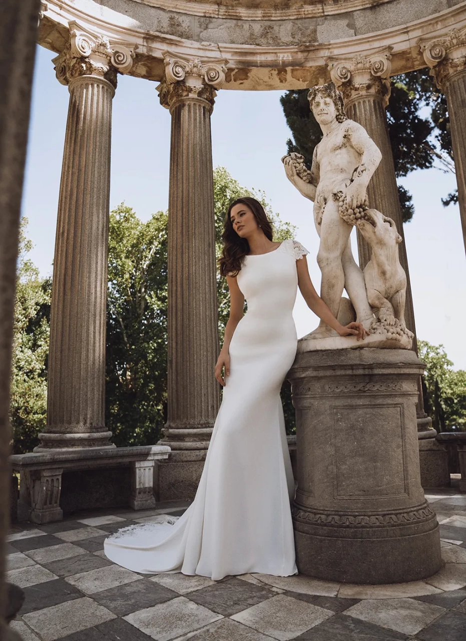 Abito da sposa con maniche corte in pizzo effetto tattoo, schiena scoperta, scollo a barchetta, strascico particolare con lavorazione in pizzo