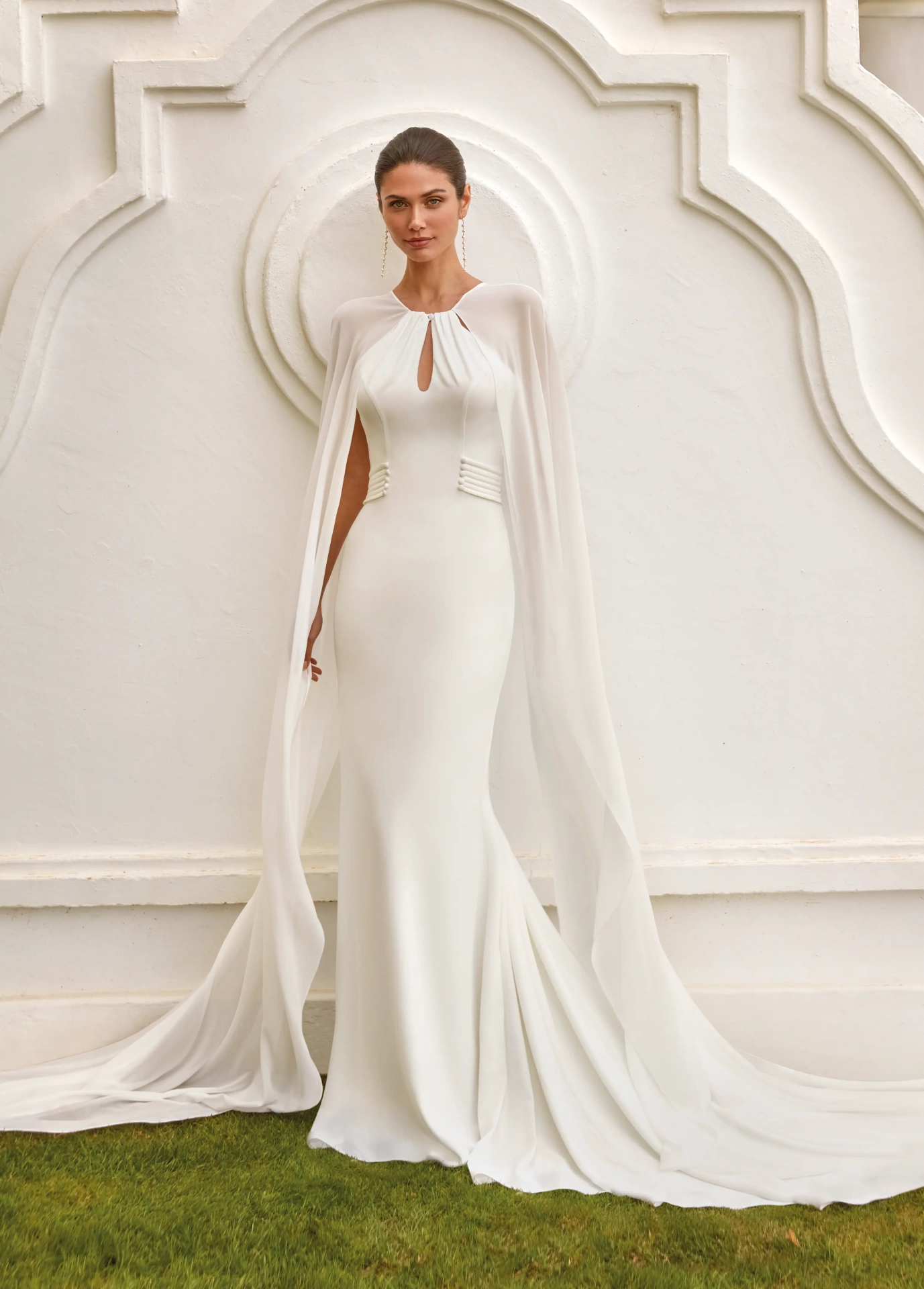 Abito da sposa elegante e raffinato a sirena con scollo all'americana, schiena scoperta, maniche particolari in chiffon che creano un mantello a strascico lungo fino a terra, applicazioni di perle sui fianchi