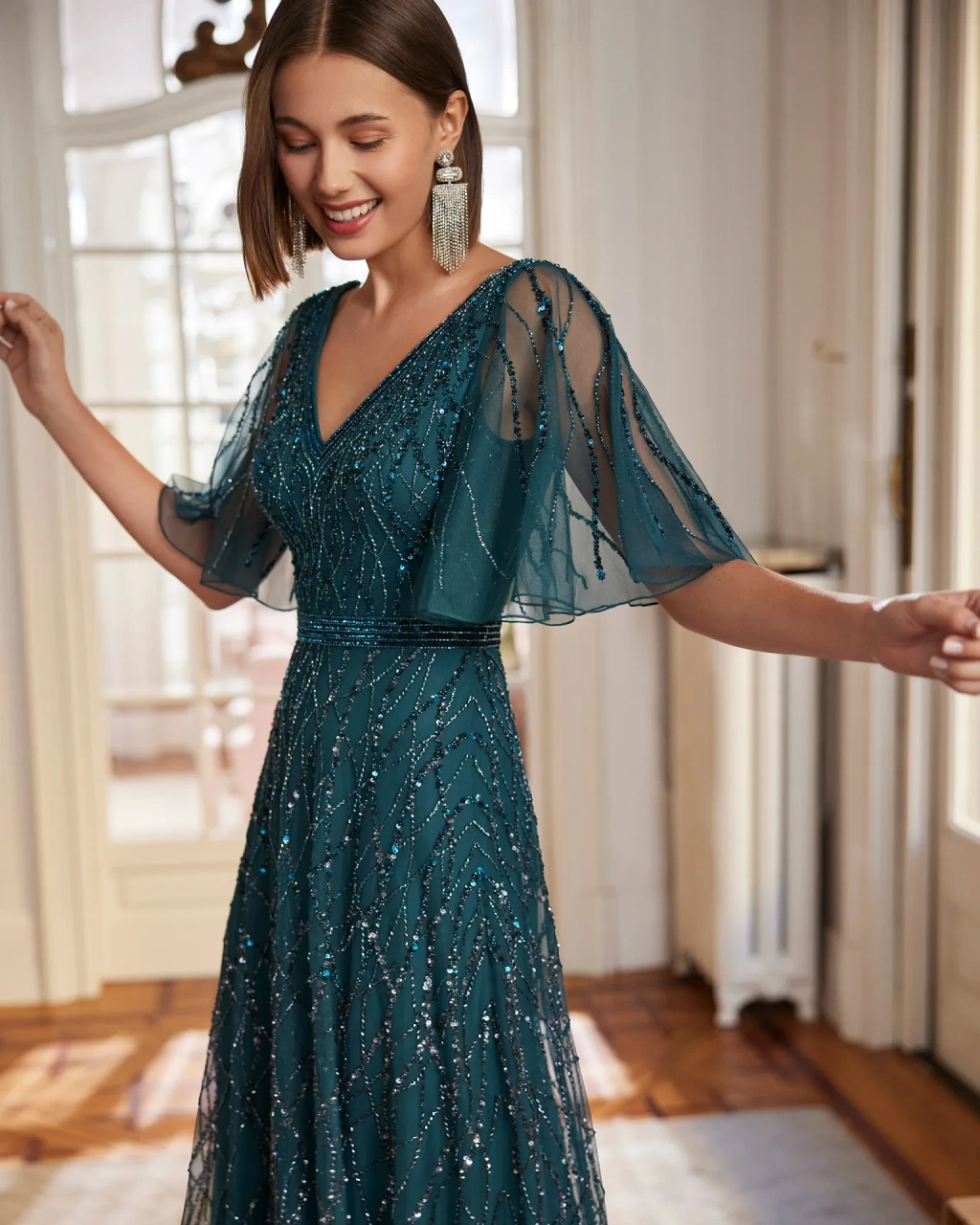 Abito da cerimonia lungo verde scuro A-line con scollo a V sia davanti che dietro, maniche corte velate a campana, trama con applicazioni di strass e glitter su tutta la silhouette - Lo Specchio Sposi Atelier Abiti da Cerimonia a Verona