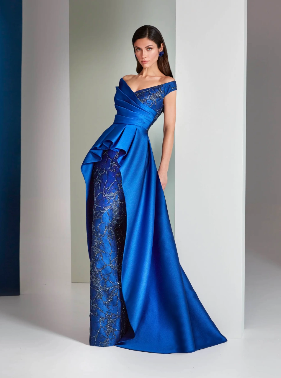 Abito da cerimonia blu cobalto lungo perfetto per mamma della sposa o dello sposo, scollo a V off-shoulder con corpino drappeggiato, gonna a sirena con trama dorata e sovragonna asimmetrica che accentua e valorizza il punto vita - Lo Specchio Atelier Abiti da Cerimonia a Verona