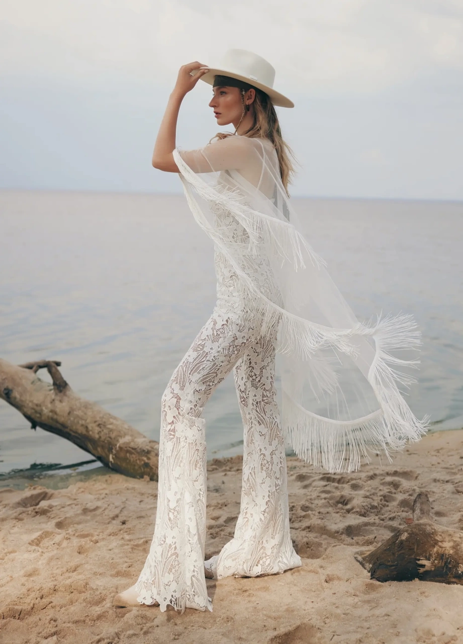 Tuta da sposa particolare stile boho in pizzo effetto tattoo, aderente, pantaloni a zampa, scollo a cuore senza spalline, kimono in tulle trasparente con frange stile country