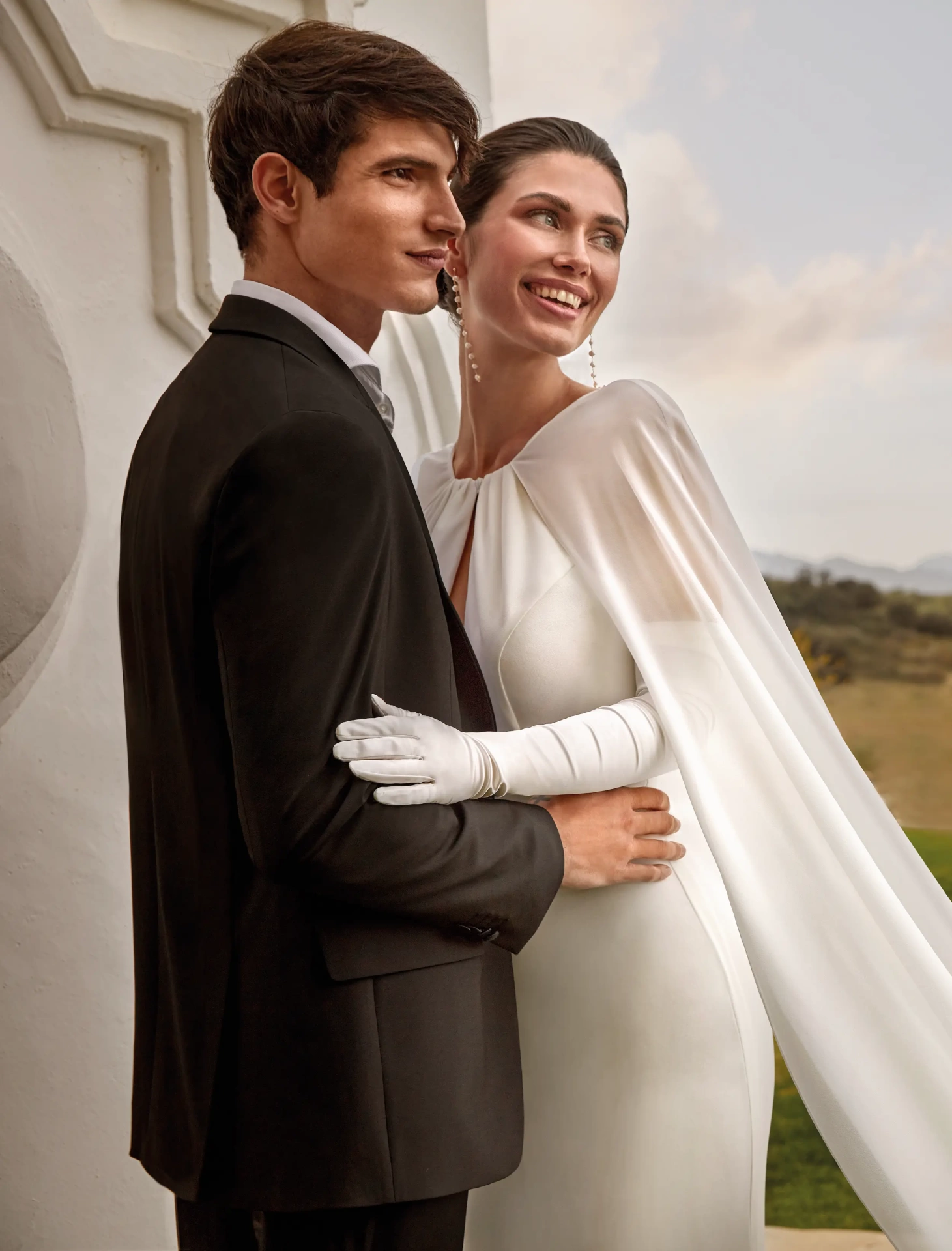 Abito da sposa elegante e raffinato a sirena con scollo all'americana, schiena scoperta, maniche particolari in chiffon che creano un mantello a strascico lungo fino a terra, applicazioni di perle sui fianchi