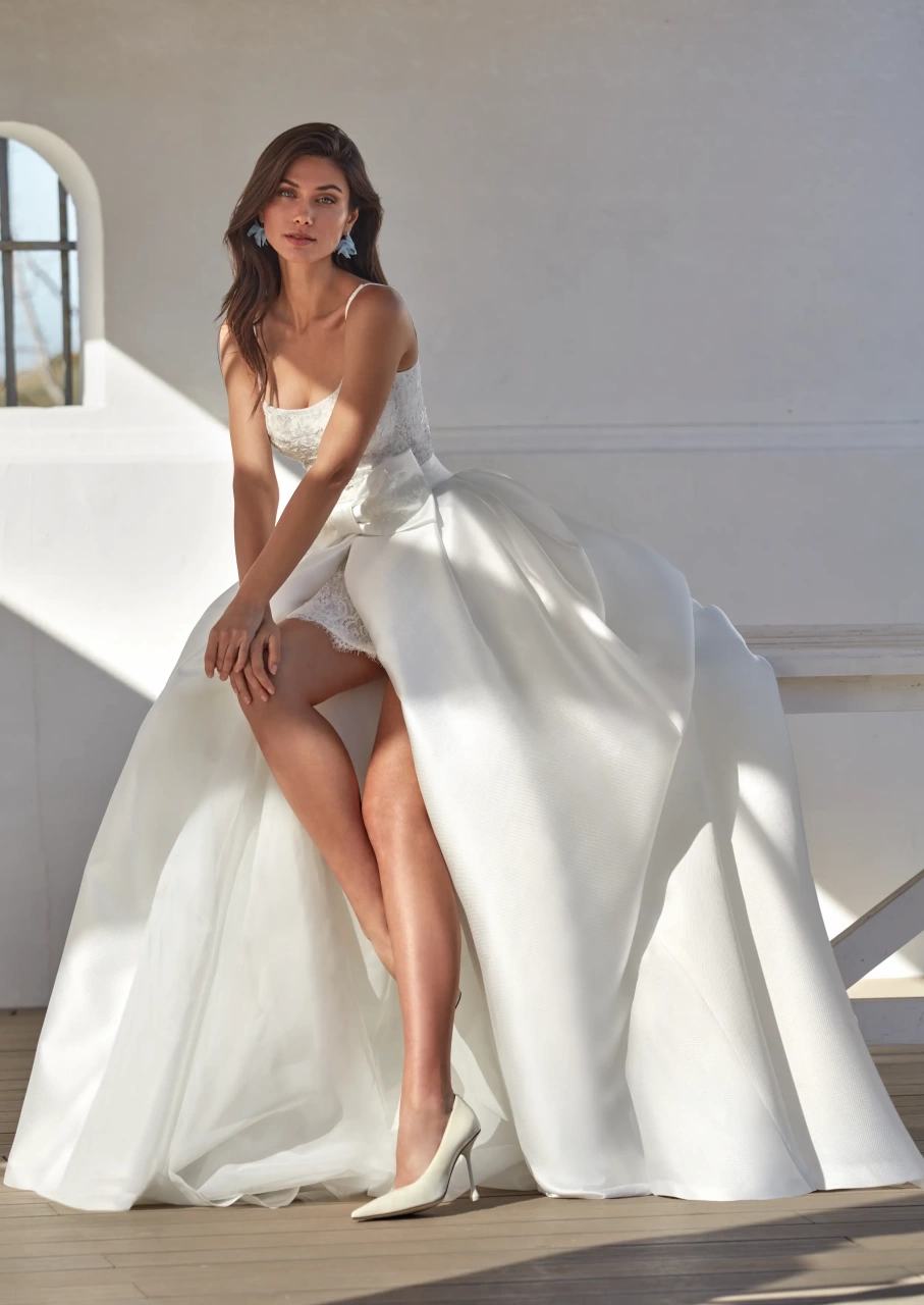 Vestito da sposa corto in pizzo con scollo squadrato e spalline spesse, gonna staccabile ampia e strutturata in mikado con fiocco frontale in pizzo