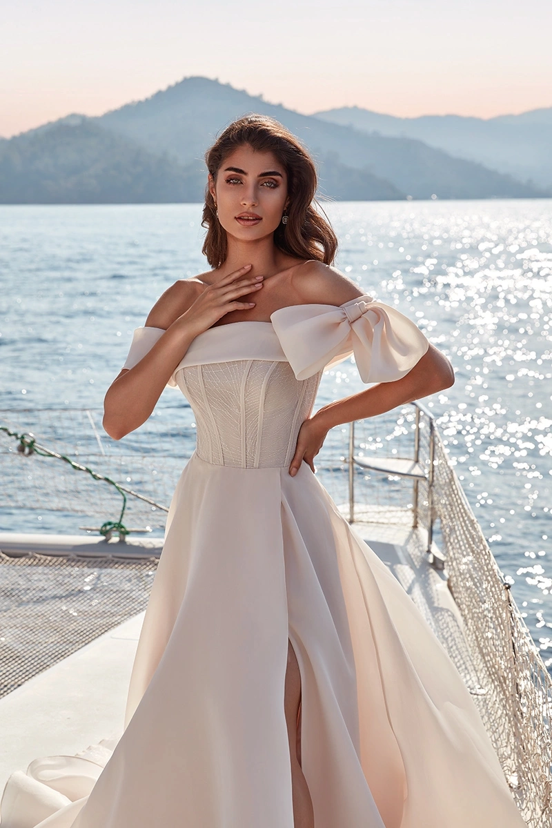 Abito da sposa classico semplice elegante e raffinato con scollo dritto off-shoulder, fiocco strutturato sulla spallina sinistra, corsetto con stecche a vista e lavorazione di piccoli glitter e cristalli, gonna scivolata in organza con spacco a portafoglio | Lo Specchio Atelier Abiti da Sposa a Verona