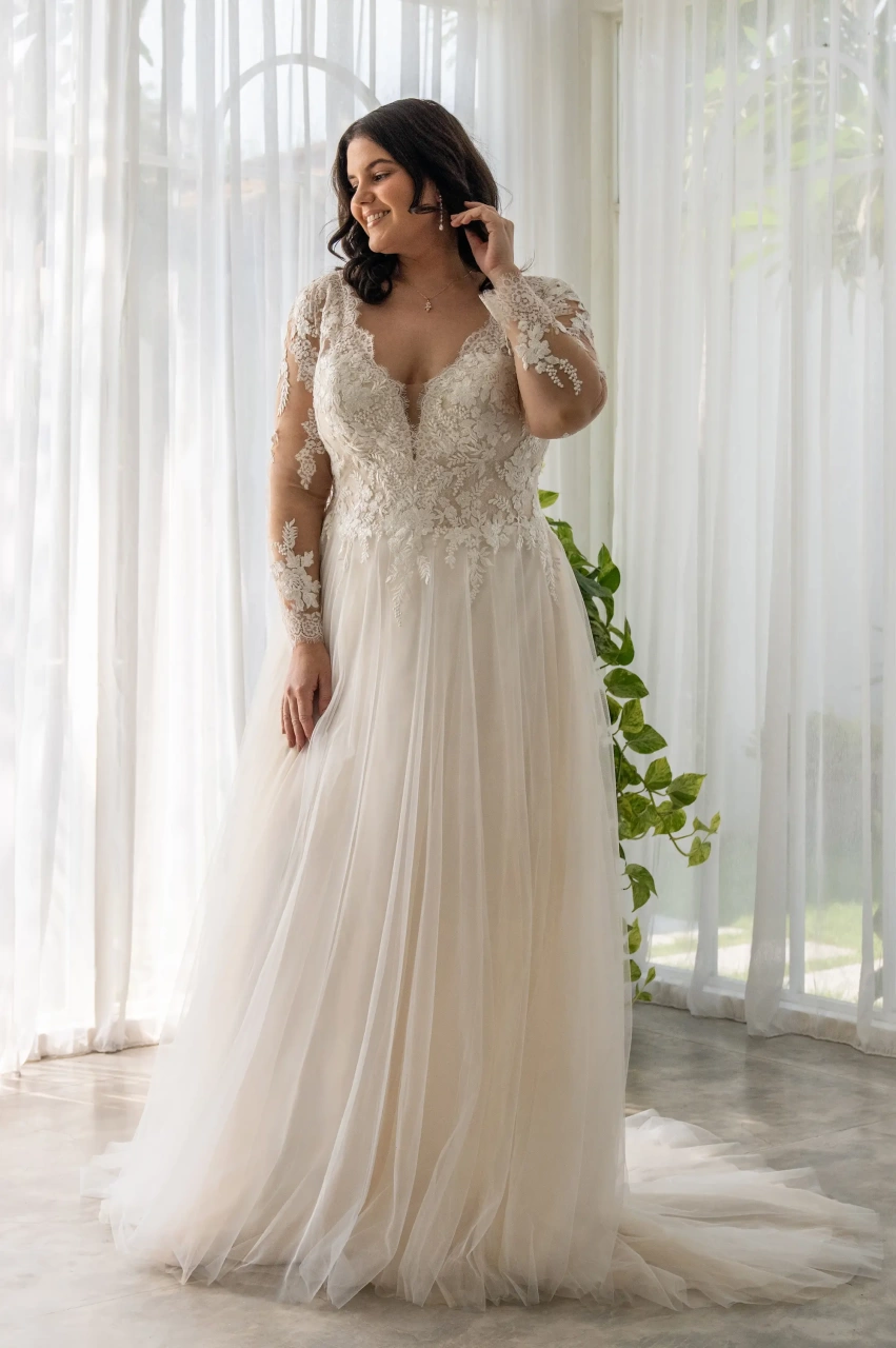 Abito da sposa curvy e taglie forti con maniche lunghe in pizzo effetto tattoo, corpino in pizzo con scollo profondo a V, gonna A-line scivolata in tulle drappeggiato, schiena scoperta | Lo Specchio Atelier Abiti da Sposa a Verona