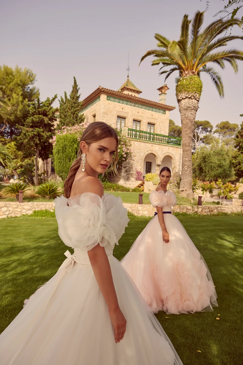 Abito da sposa particolare colorato rosa lussuoso e principesco in tulle, scollo off-shoulder con grandi rose di tulle applicate sia davanti che sulla schiena, fascia in raso viola in vita, gonna ampia in tulle con lavorazione di grandi rose tridimensionali di tulle, disponibile anche in bianco | Lo Specchio Atelier Abiti da Sposa a Verona