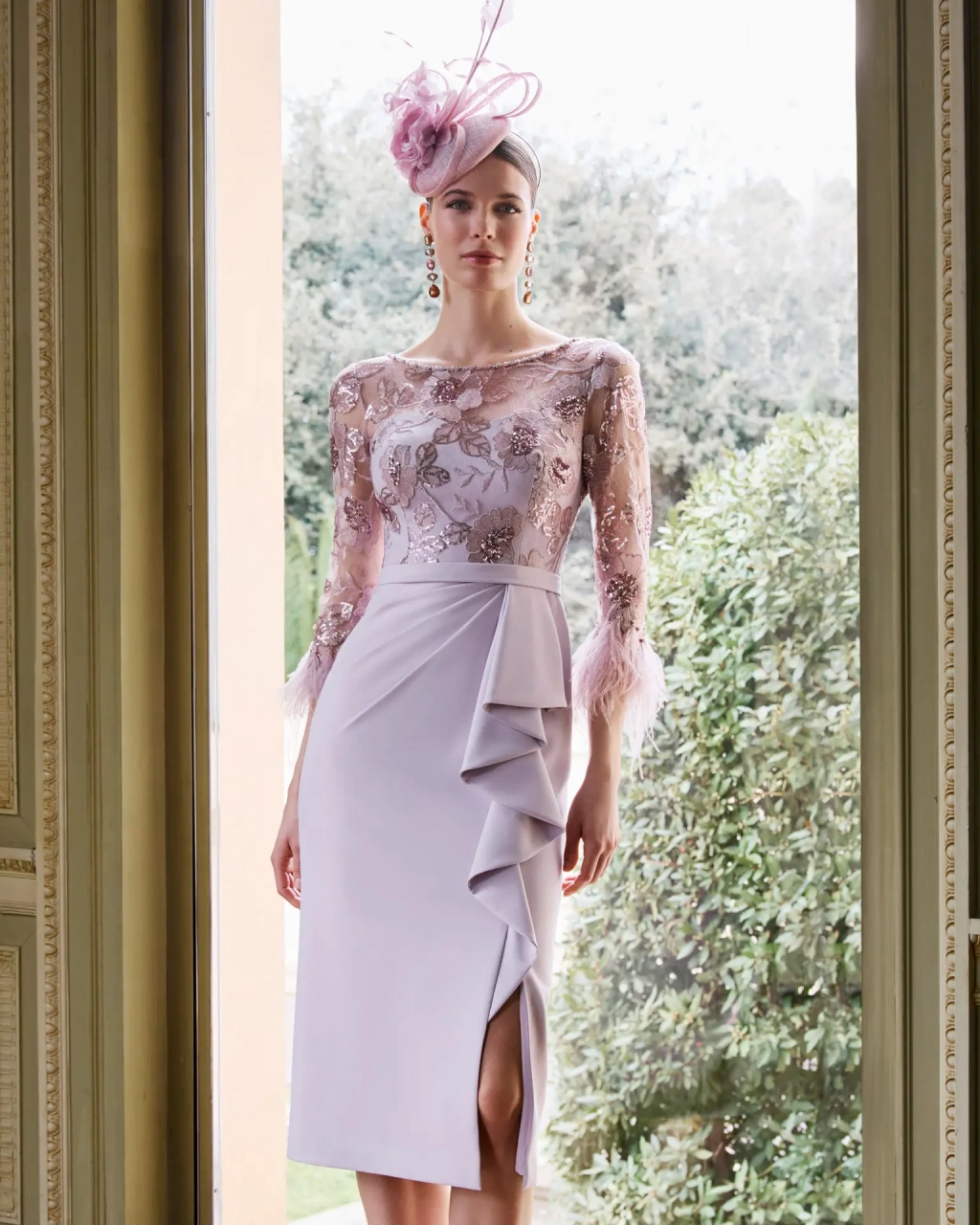 Abito da cerimonia con manica lunga e gonna a tubino perfetto per la mamma della sposa o dello sposo, color rosa e lilla, drappeggio 3D sulla gonna con elegante spacco al ginocchio, corpino velato con pizzo di strass e diamanti e applicazioni di piume rosa sulle maniche - Lo Specchio Atelier Abiti da Cerimonia a Verona