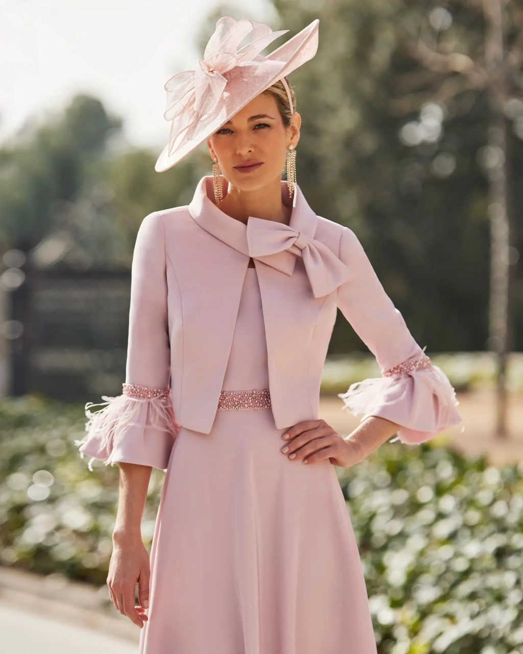 Abito da cerimonia per la mamma della sposa o dello sposo, rosa cipria, gonna midi scivolata, maniche corte, fascia strass ton-sur-ton in vita, bolerino strutturato sartoriale con fiocco 3D sul collo e maniche eleganti con dettagli applicati - Lo Specchio Atelier Abiti da Cerimonia a Verona