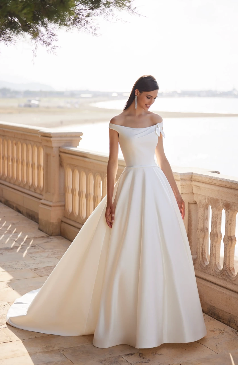 Vestito da sposa semplice elegante e raffinato A-line in mikado, gonna ampia strutturata, scollo off-shoulder con piccolo drappeggio che forma un fiocco sulla spallina sinistra | Lo Specchio Atelier Vestiti da Sposa a Verona