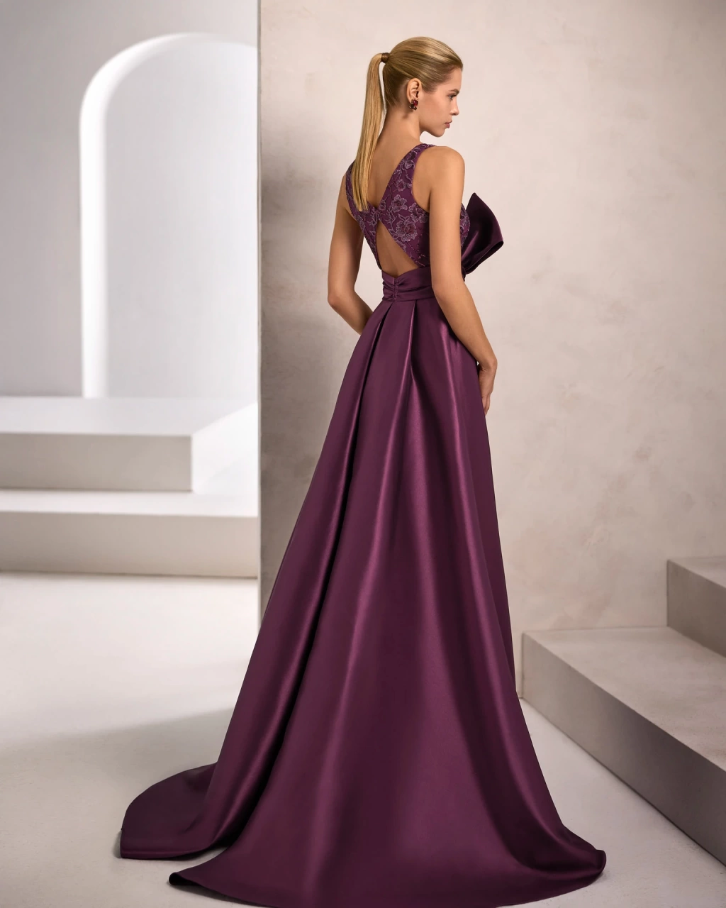 Vestito da cerimonia elegante da donna lungo viola in pizzo floreale, scollo profondo a V e spalline larghe, con sovragonna ampia in mikado viola con fiocco scenografico sul punto vita - Lo Specchio Atelier Abiti da Cerimonia a Verona