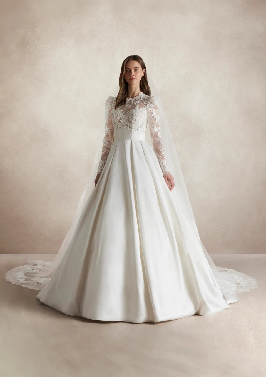 Abito da sposa particolare con maniche lunghe a sbuffo in pizzo effetto tattoo, scollo rotondo, gonna ampia A-line drappeggiata in mikado con fiocco drappeggiato sulla schiena e strascico lungo