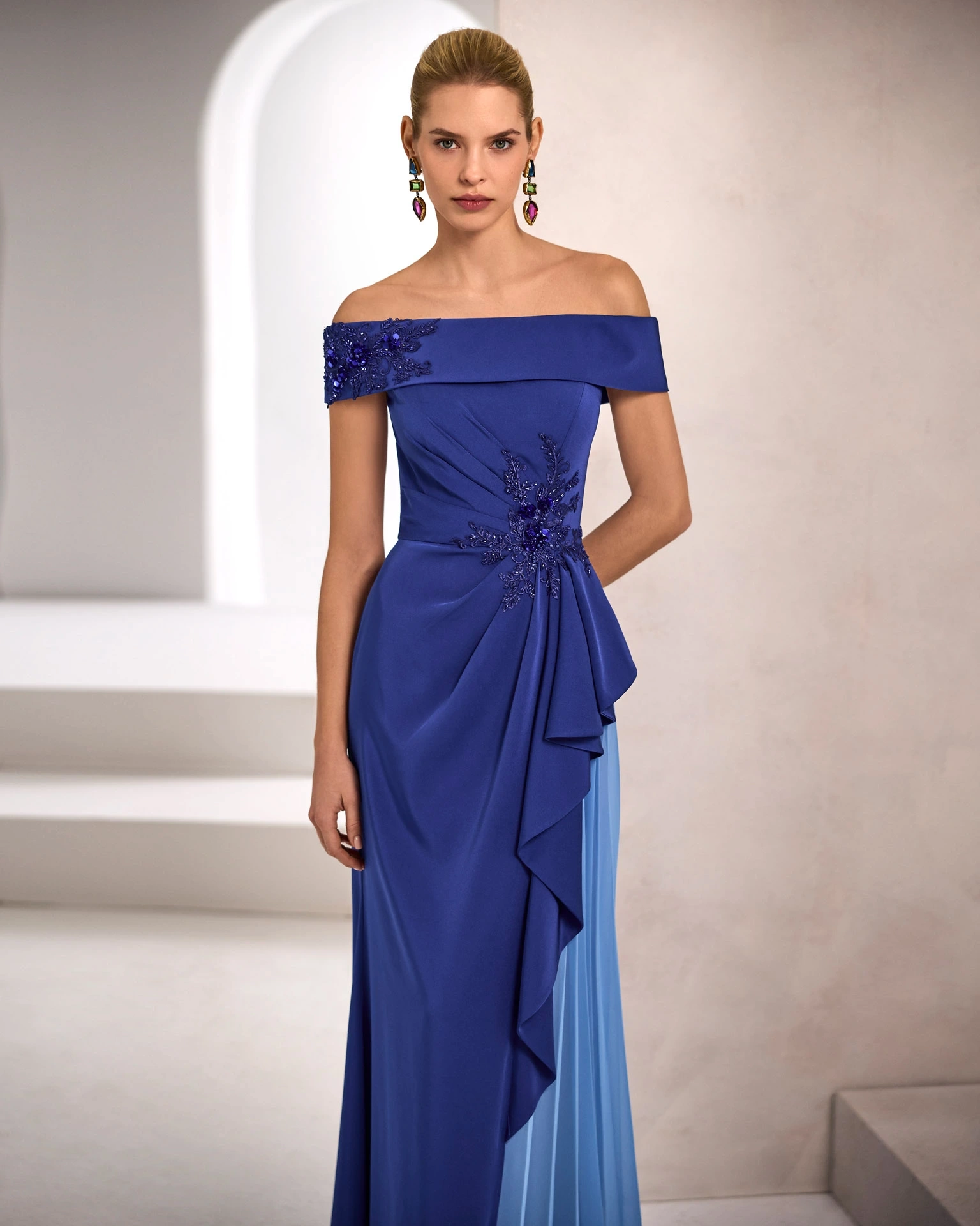 Vestito da cerimonia donna lungo blu, scollo off-shoulder strutturato, drappeggio sul punto vita e gonna asimmetrica a contrasto, applicazioni 3D di pizzo floreale sulla spalla destra e sul corpetto - Lo Specchio Atelier Abiti da Cerimonia a Verona