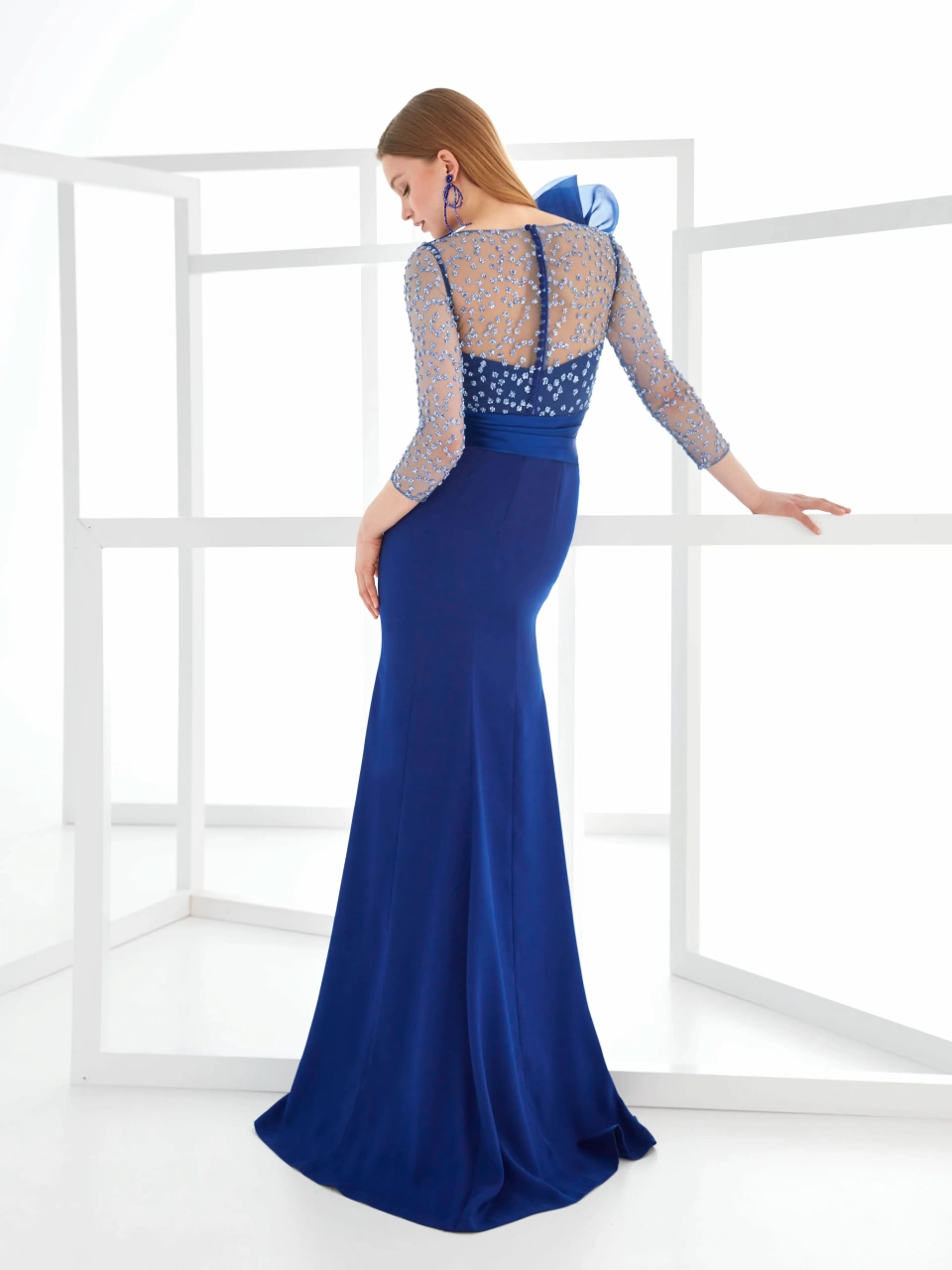 Abito da cerimonia blu elettrico con maniche lunghe velate con applicazioni di cristalli, silhouette a sirena, scollo a barchetta con dettaglio velato, fascia drappeggiata sul punto vita, ruches 3D voluminose e scenografiche sulla spalla destra - Lo Specchio Atelier Abiti da Cerimonia a Verona