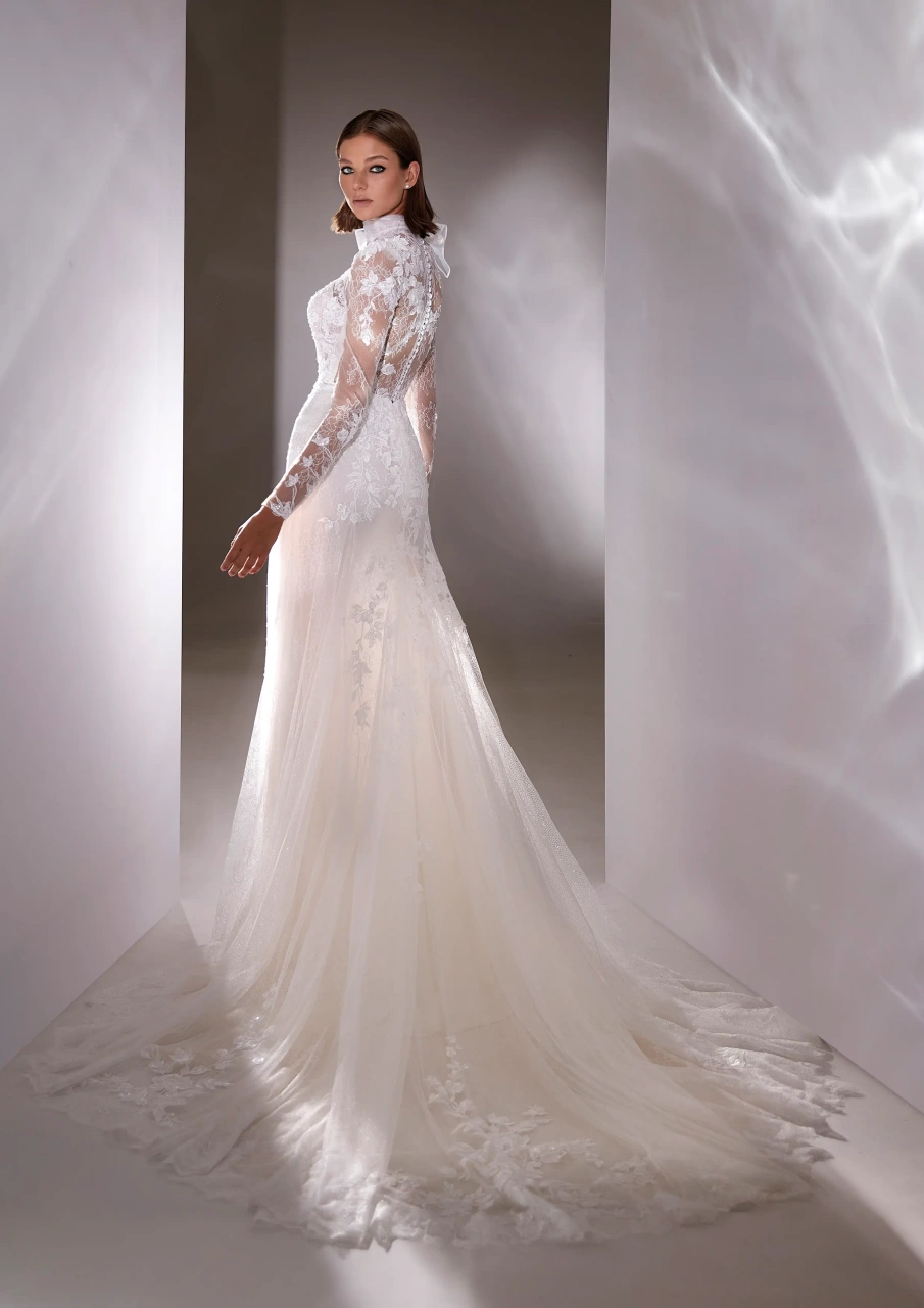 Abito da sposa con maniche lunghe in pizzo, collo alto con fiocco in tulle, corpino steccato, gonna scivolata aderente in tulle con applicazioni di pizzo floreale | Lo Specchio Atelier Abiti da Sposa a Verona